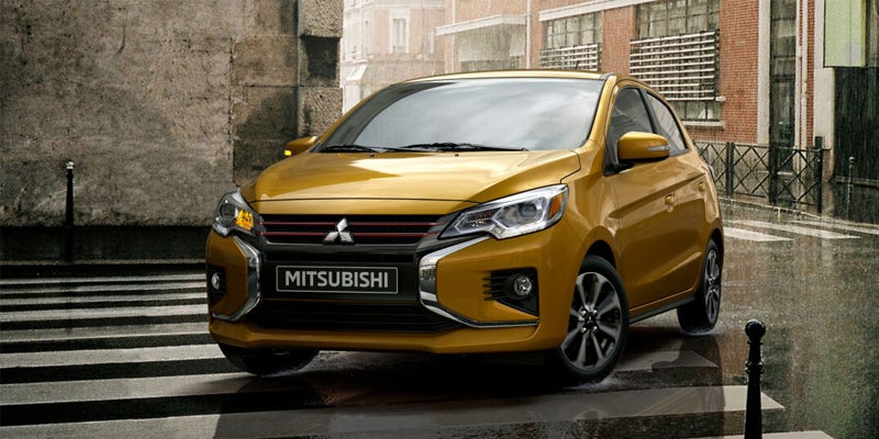 brand new mustard yellow 2023 Mitsubishi Mirage taking a turn, crossing over a crosswalk on a city street, in the rain.