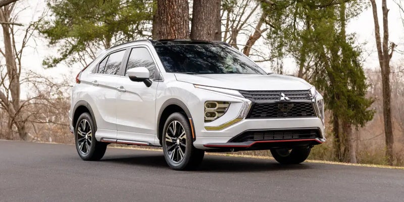 a brand new white Mitsubishi Eclipse Cross driving on backroad forest highway roads.